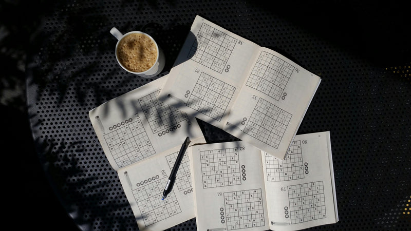 Sudoku puzzles on a table with a cup of coffee and a pen.